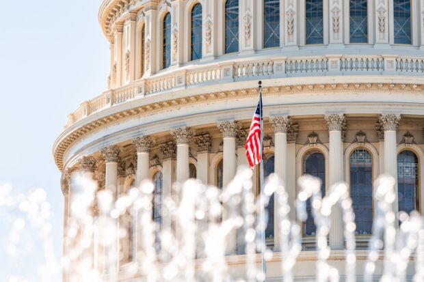 US Congress dome with foreground of water fountain splashing and American flag waving in Washington DC on capitol hill