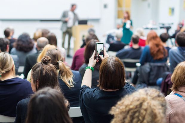 Student holding up phone in lecture. To illustrate concern about views expressed in class being shared on social media. Student holding up phone in lecture. To illustrate concern about views expressed in class being shared on social media.