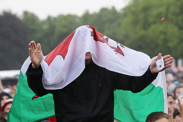 A Wales fan in the rain with flag covering his head. To illustrate that changes to student finance pledged by the front runners in the upcoming Welsh election may be unworkable.