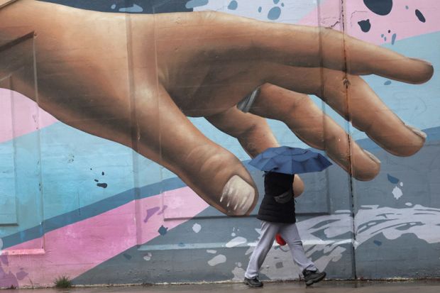 Wall art of hand reaching out with person walking by holding an umbrella in Toronto Wall art of hand reaching out with person walking by holding an umbrella in Toronto to illustrate How to meet students’ soaring mental health needs on a budget