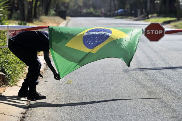 A security guard tries to tie down a Ukraine-flag over a stop sign on a barrier to illustrate Open access is closed to middle-income nations too rich for fee waivers
