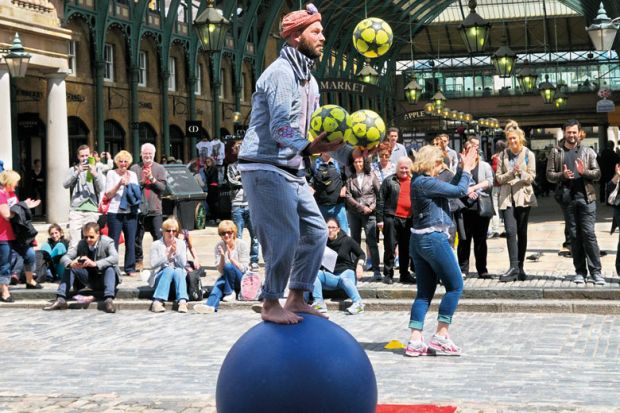 Street performer entertaining people balancing on a ball  in Covent Garden Piazza to illustrate Russell Group draws majority of fee income from overseas