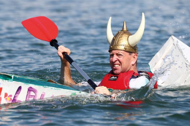 Person wearing viking hat in a cardboard boat sinking at a boat Regatta Person wearing viking hat in a cardboard boat sinking at a boat Regatta to illustrate the Danish humanities courses pressed on contact hours as funding cut