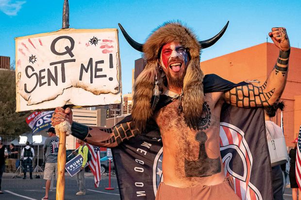 Jake Angeli, 33, aka Yellowstone Wolf, from Phoenix, holds a QAnon sign, as he presents himself as a shamanist and consultant for the Trump supporters gathered in front of the Maricopa County Election Department where ballots are counted after the US pres Jake Angeli, 33, aka Yellowstone Wolf, from Phoenix, holds a QAnon sign, as he presents himself as a shamanist and consultant for the Trump supporters gathered in front of the Maricopa County Election Department where ballots are counted after the US pres