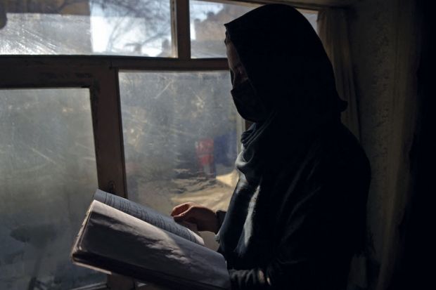 Marwa, a student at her home in Kabul reading next to a window as women are now banned from attending university in Taliban