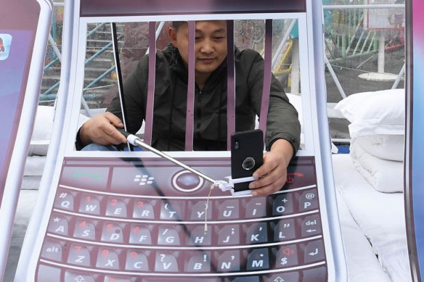 Person with arms behind art installation bars holding his mobile phone other side of bars