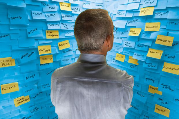 Man standing in front of wall covered in sticky notes Middle-aged man standing in front of wall covered in sticky notes to illustrate Big HE ideas are plentiful. Why aren’t v-cs listening?