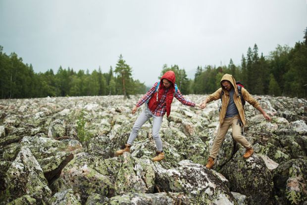 Young tourists walking down big stones while hiking