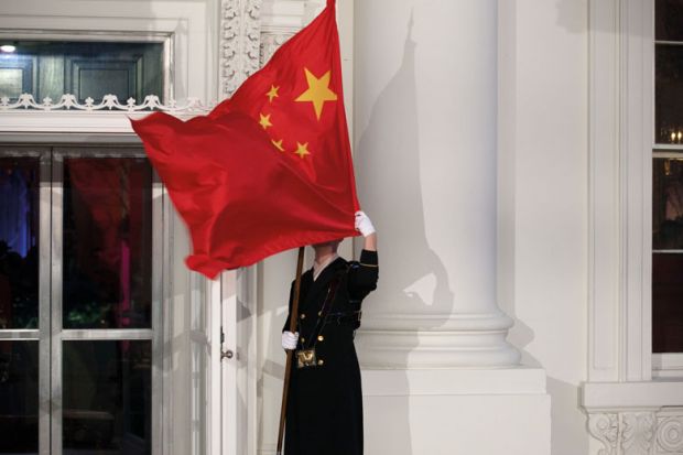 A military honor guard holds the Chinese flag in front of the White House in Washington which has blown over his face to illustrate Republicans target universities over China and political research