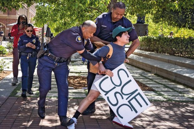 Holding a sign that said Sue USC a USC student is arrested by campus police in USC Village after calling for USC to sued and held accountable for their actions surrounding the pro-Palestinian protest on campus on Monday, May 6, 2024 in Los Angeles, CA 