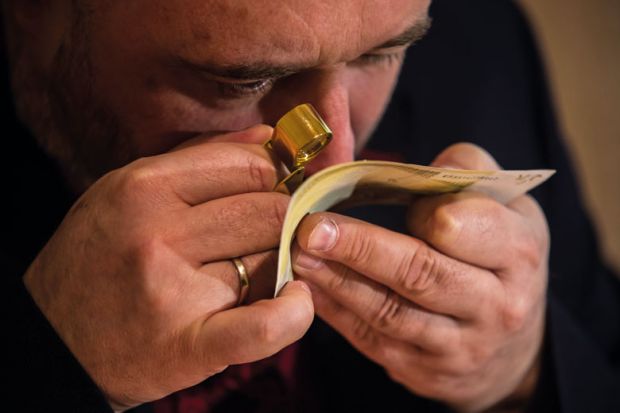 An employee examines with magnifier glass counterfeit 200 Euro bank note to illustrate Problems with bank checks drive student visa refusals
