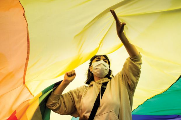 Person standing under an LGBT flag. Person standing under an LGBT flag as a metaphor for Melbourne revises free speech rules over transgender concerns.