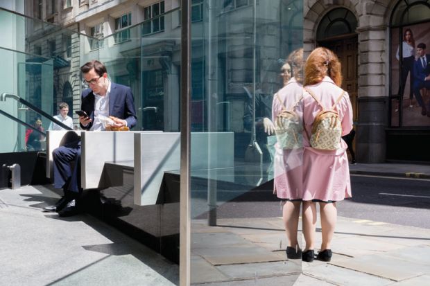 Businessman inside building looking at phone, woman standing outside as a metaphor for gender split: degrees aren’t paying off for women