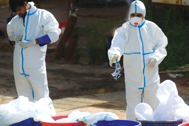 Two medical staff removing Personal Protective Equipment kits into a dustbin as a metaphor for universities reprioritising teaching over research.