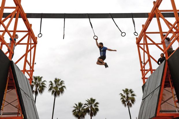 man swings across obstacle course