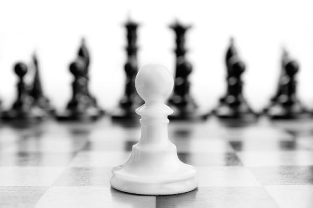 White chess pawn with black pieces in background White chess pawn with black pieces in background