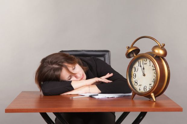 Woman asleep on desk with large alarm clock Woman asleep on desk with large alarm clock