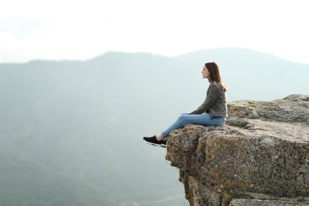 A woman sits on the edge of a cliff