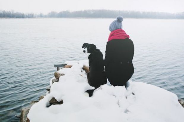 Woman and dog sitting on a snowy river bank