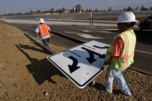 Workmen carrying traffic sign along roadside Workmen carrying traffic sign along roadside